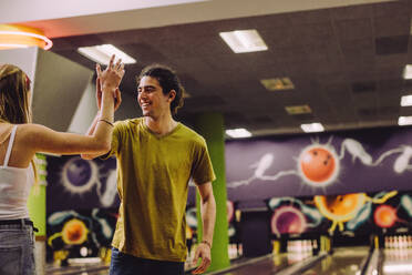 Fröhlicher junger Mann und Frau schauen sich an und geben sich nach einem Strike auf der Bowlingbahn ein High-Five. - JLPSF24753