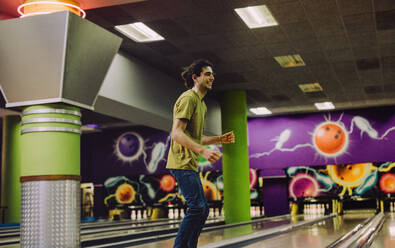 Glücklicher junger Mann auf der Bowlingbahn nach dem Werfen der Kugel. Mann spielt auf der Bowlingbahn. - JLPSF24754