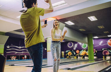 Junger Mann nimmt Frau auf, die in einem Club Bowling spielt. Junge Freunde genießen es, in einer Bowling-Arena zu spielen. - JLPSF24756
