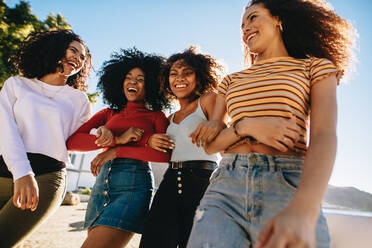 Vier junge Frauen, die zusammen am Strand spazieren gehen. Mehrrassige Freundinnen an einem Sommertag am Strand. - JLPSF24758