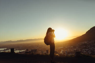 Frau mit Kamera, die eine Landschaft fotografiert. Weibliche Reisende, die Bilder von einem Berggipfel bei Sonnenuntergang schießt. - JLPSF24777