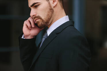 Businessman talking over mobile phone. Young business professional looking busy talking on mobile phone outdoors. - JLPSF24797