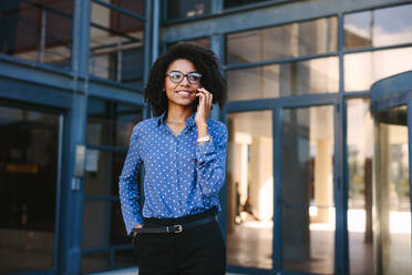 Businesswoman standing outside office building talking on cell phone. Business professional making a phone call while standing outdoor. - JLPSF24817