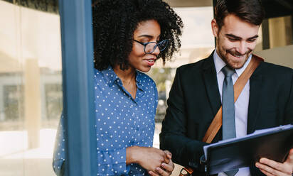 Two business professionals looking at a file and smiling. Office colleagues walking together and discussing over a business report. - JLPSF24824