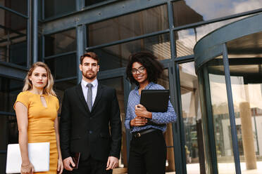 Portrait of confident business people standing together in front of office building. Group of multi-ethnic business colleagues looking at camera. - JLPSF24831