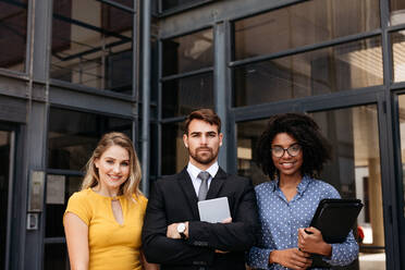 Group of young corporate professionals standing together and looking at camera. Multiracial business people standing in front of office building. - JLPSF24835