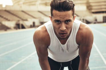 Close up of a runner standing on a running track resting his hands on knees. Athlete relaxing after a run standing on the track. - JLPSF24885