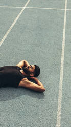 Runner lying on the track in a relaxed mood with hands under his head. Top view of an athlete relaxing after a run. - JLPSF24888