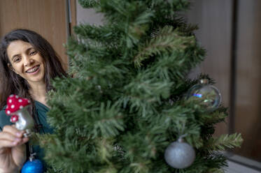 Glückliche Frau beim Schmücken des Weihnachtsbaums zu Hause - ANAF00328