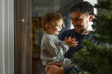Happy father with son looking at Christmas decoration at home - ANAF00337