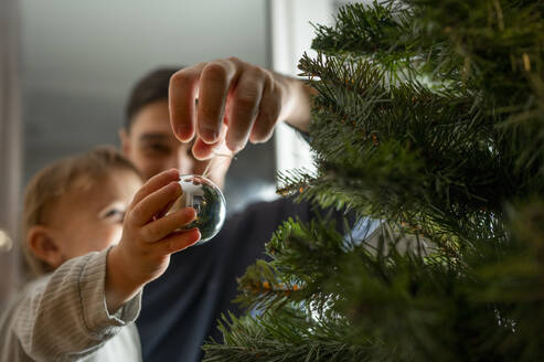 Junge mit Vater beim Schmücken des Weihnachtsbaums zu Hause - ANAF00338