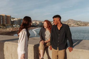 Lachende Freunde am Meer. Drei multikulturelle Freunde lachen und amüsieren sich am Strand. Eine Gruppe fröhlicher junger Leute, die am Wochenende zusammen abhängen. - JLPSF24921