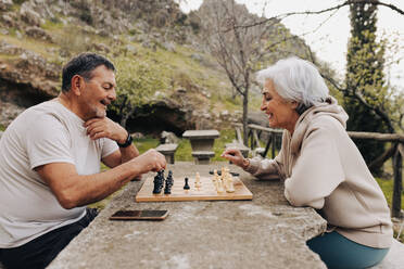 Ein älteres Paar im Ruhestand spielt zusammen Schach in einem Park. Ein glückliches älteres Paar verbringt nach der Pensionierung einige schöne Stunden miteinander. Ein reifes Paar, das sich im Freien amüsiert. - JLPSF25061