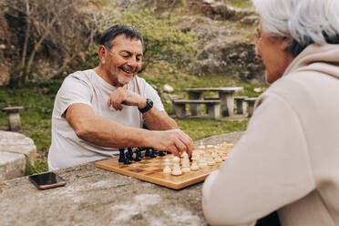 Unbeschwertes älteres Paar, das im Park Schach spielt. Glückliches älteres Paar, das nach der Pensionierung Zeit miteinander verbringt. Älteres Paar, das sich im Freien amüsiert. - JLPSF25062