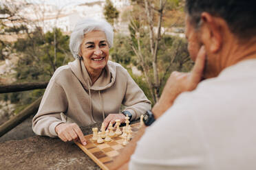 Ehepaar im Ruhestand spielt eine Partie Schach in einem Park. Fröhliches älteres Ehepaar, das nach der Pensionierung viel Zeit miteinander verbringt. Glückliches älteres Ehepaar, das sich im Freien vergnügt. - JLPSF25065