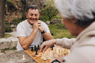 Älteres Paar, das in einem Park eine Partie Schach spielt. Fröhliches älteres Paar, das nach dem Eintritt in den Ruhestand einige schöne Stunden miteinander verbringt. Älteres Paar, das sich im Freien amüsiert. - JLPSF25066