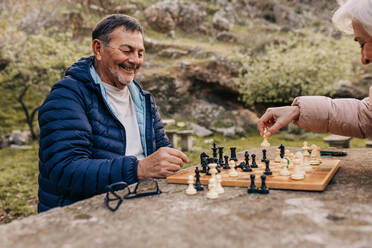 Fröhliches älteres Paar, das in einem Park eine Partie Schach spielt. Fröhliches älteres Paar, das nach der Pensionierung viel Zeit miteinander verbringt. Reifes Paar, das sich im Freien vergnügt. - JLPSF25072