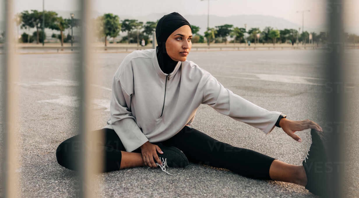 Young barefoot woman in leggings and pullover stretching legs during  exercise Stock Photo