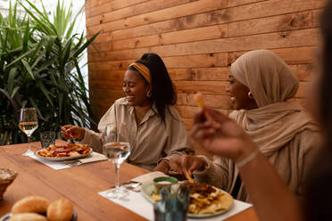 Fröhliche Freundinnen, die eine gesunde Mahlzeit in einem Restaurant genießen. Eine Gruppe multikultureller Freunde beim gemeinsamen Mittagessen in einer Cafeteria. Millennial-Freunde, die am Wochenende zusammen abhängen. - JLPSF25161