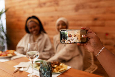 Junge Frau, die ein Foto von ihren Freunden in einem Restaurant macht. Multikulturelle Freundinnen beim gemeinsamen Mittagessen in einer Cafeteria. Millennial-Freunde, die Inhalte für ihren Social-Media-Blog erstellen. - JLPSF25167