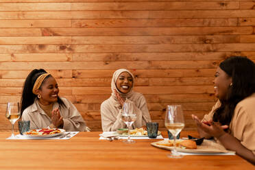 Freunde feiern eine Verlobung in einem Restaurant. Glückliche junge Frauen gratulieren ihrer muslimischen Freundin zu ihrer neuen Verlobung. Drei multikulturelle Freundinnen beim gemeinsamen Mittagessen. - JLPSF25177