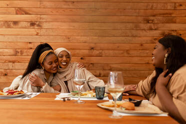 Unterstützende Freundinnen, die ihrer muslimischen Freundin zu ihrer Verlobung gratulieren. Gruppe glücklicher junger Frauen, die in einem Restaurant eine Verlobung feiern. Drei multikulturelle Freunde beim gemeinsamen Mittagessen. - JLPSF25179