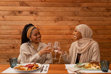 Prost auf unsere gesunde Freundschaft. Zwei glückliche Freundinnen stoßen in einem Restaurant an. Zwei unterschiedliche junge Frauen, die am Wochenende ein gemütliches Mittagessen zusammen genießen. - JLPSF25186