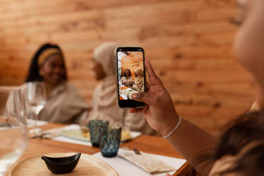 Millennial woman taking a picture of her friends in a restaurant. Multicultural female friends having lunch together in a cafeteria. Cheerful young friends making happy memories together. - JLPSF25194