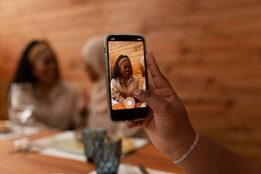 Frau, die ein Foto von ihren Freunden in einem Restaurant macht. Multikulturelle Freundinnen beim gemeinsamen Mittagessen in einer Cafeteria. Fröhliche Millennial-Freundinnen, die gemeinsam glückliche Erinnerungen schaffen. - JLPSF25195