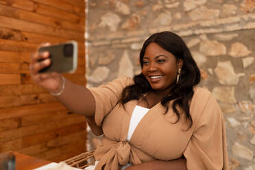 Happy young woman taking a selfie while sitting in a restaurant. Cheerful young woman having lunch alone in a cafeteria. Millennial woman capturing happy moments on the weekend. - JLPSF25199