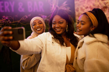 Diverse girlfriends taking a selfie in a restaurant. Happy young women smiling for a group photo while standing together. Multicultural young friends enjoying a reunion on the weekend. - JLPSF25202