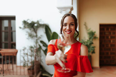 Smiling woman making a toast with sparkling wine. Happy young woman celebrating while standing outside a holiday home. Cheerful young woman having a good time on the weekend. - JLPSF25251