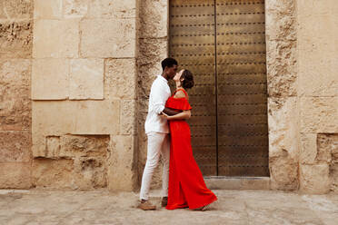 Couple sharing a passionate kiss on a vacation. Affectionate young couple sharing an intimate moment while standing in front of an antique building. Interracial couple enjoying their weekend getaway. - JLPSF25259