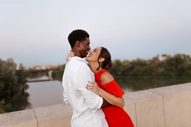 Carefree young couple laughing while standing on a bridge. Happy interracial couple embracing each other affectionately. Romantic young couple having a good time during their vacation. - JLPSF25266