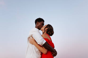 Passionate couple kissing with the sky in the background. Affectionate young couple sharing an intimate moment on a vacation. Young interracial couple enjoying their weekend getaway. - JLPSF25270