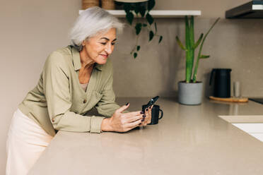 Retired mature woman taking a video call in her kitchen at home. Grey-haired senior woman communicating with her loved ones using wireless technology. - JLPSF25278