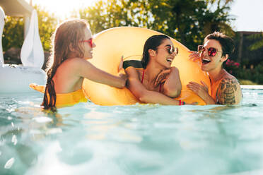 Girls enjoying a day in swimming pool with inflatable ring. Smiling women friends having fun in pool. - JLPSF25306