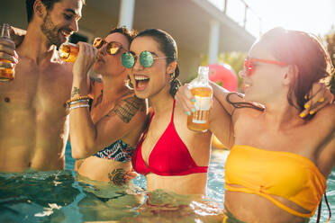 Multirassische Gruppe von Freunden, die sich auf einer Poolparty amüsieren. Eine Gruppe von Männern und Frauen trinkt und genießt zusammen im Schwimmbad. - JLPSF25307