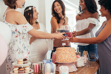 Glückliche multiethnische Freunde stoßen bei einer Babyparty an. Eine Gruppe von Freunden feiert eine Babyparty mit Säften. - JLPSF25314