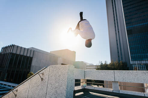 Athletic man practicing parkour and free running by doing a frontflip from a obstacle outdoors. Sporty young man practicing extreme sport activities outdoors in city. - JLPSF25329