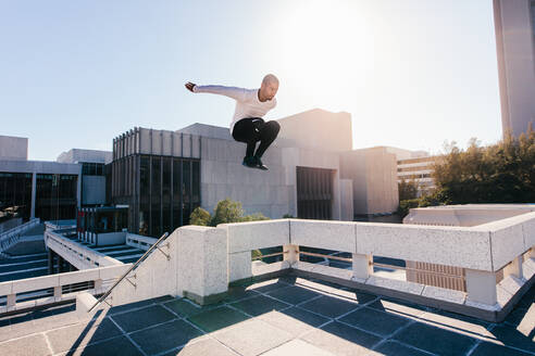 Athletic young man doing parkour tricking and freerunning over urban city background. Young sportsman practicing extreme sport activities outdoors in city. - JLPSF25330