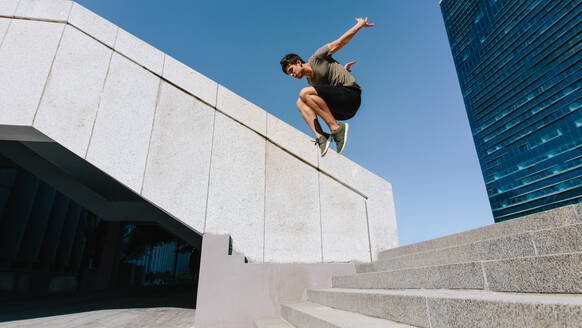 Young man jumping high over steps outdoors. Fit male free runner jumping over stairs in urban space. - JLPSF25333