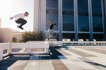 Zwei junge Sportler üben Parkour vor einem städtischen Hintergrund. Junge Menschen üben Extremsportarten im Freien in der Stadt. Männliche Athleten laufen und springen über Hindernisse. - JLPSF25341