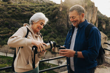 Ein glückliches älteres Paar macht eine Kaffeepause bei einer Rucksacktour im Freien. Ein fröhliches älteres Paar genießt eine gemütliche Wanderung in den Bergen. Ein abenteuerlustiges Paar verbringt nach der Pensionierung viel Zeit miteinander. - JLPSF25350