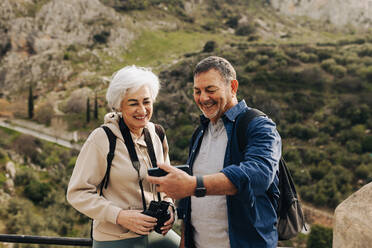 Abenteuerlustiges älteres Paar, das ein Videotelefonat führt, während es auf einem Hügel steht. Fröhliches älteres Paar, das eine erholsame Wanderung im Freien genießt. Reifes Paar, das nach der Pensionierung eine gute Zeit miteinander verbringt. - JLPSF25368