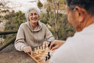 Älteres Paar, das in einem Park eine Partie Schach spielt. Fröhliches älteres Paar, das nach seiner Pensionierung einige Zeit miteinander verbringt. Glückliches älteres Paar, das sich im Freien amüsiert. - JLPSF25374