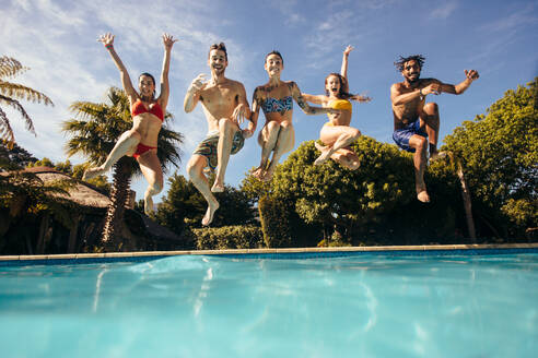 Eine Gruppe verrückter junger Leute, die in einen Swimmingpool springen, Freunde, die sich an einem Urlaubsort amüsieren. - JLPSF25385