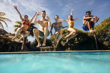 Eine Gruppe multiethnischer junger Leute sieht glücklich aus, während sie gemeinsam in den Pool springen. Freunde genießen eine Poolparty. - JLPSF25386