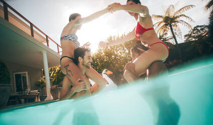 Women sitting on their boyfriends shoulders in swimming pool. Friends playing in a pool. - JLPSF25389