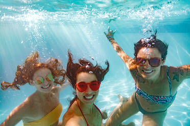 Glückliche junge Frauen Freunde schwimmen unter Wasser im Pool. Unterwasseraufnahme von lächelnden Frauen im Pool nehmen selfie. - JLPSF25391